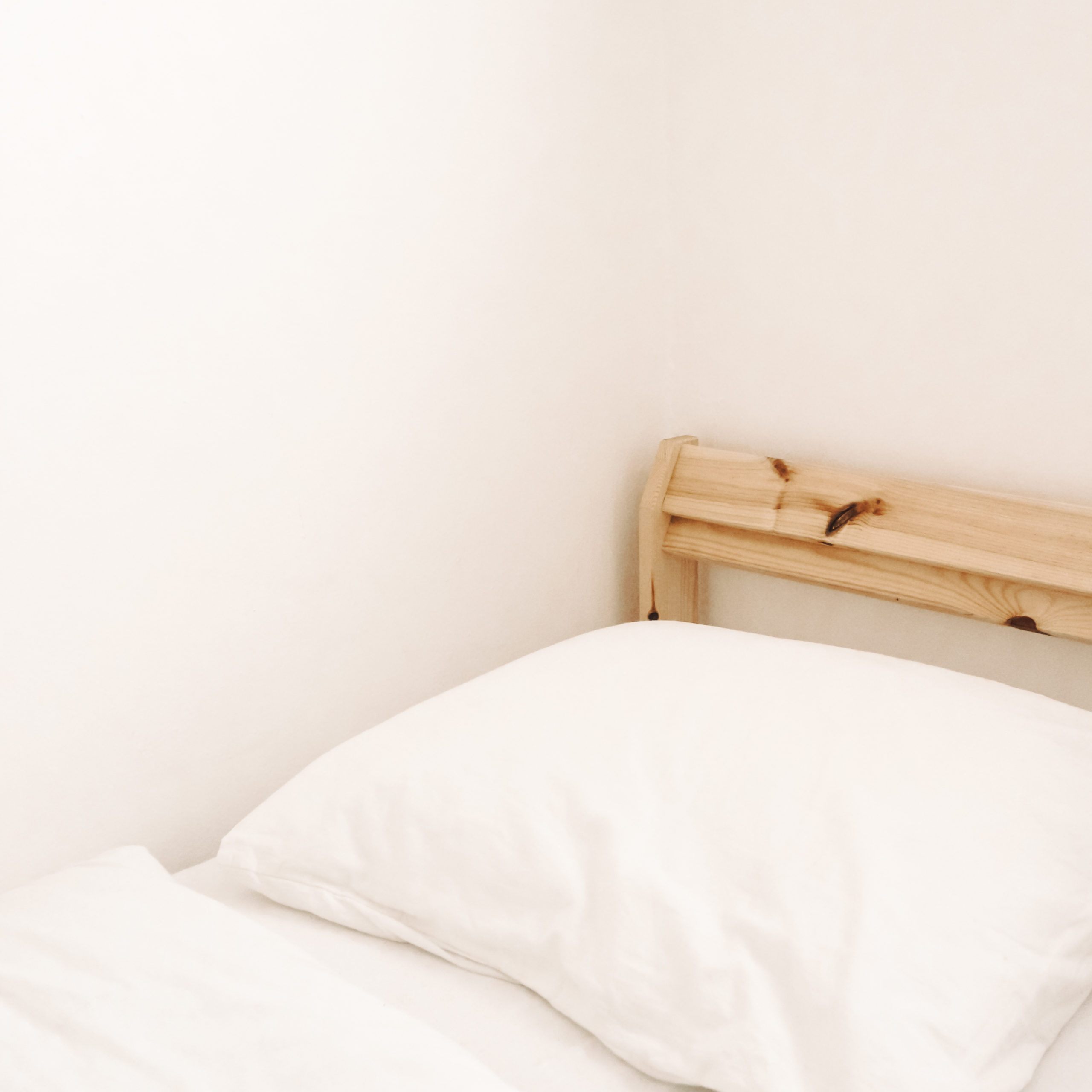 Wooden bed frame with white sheets.